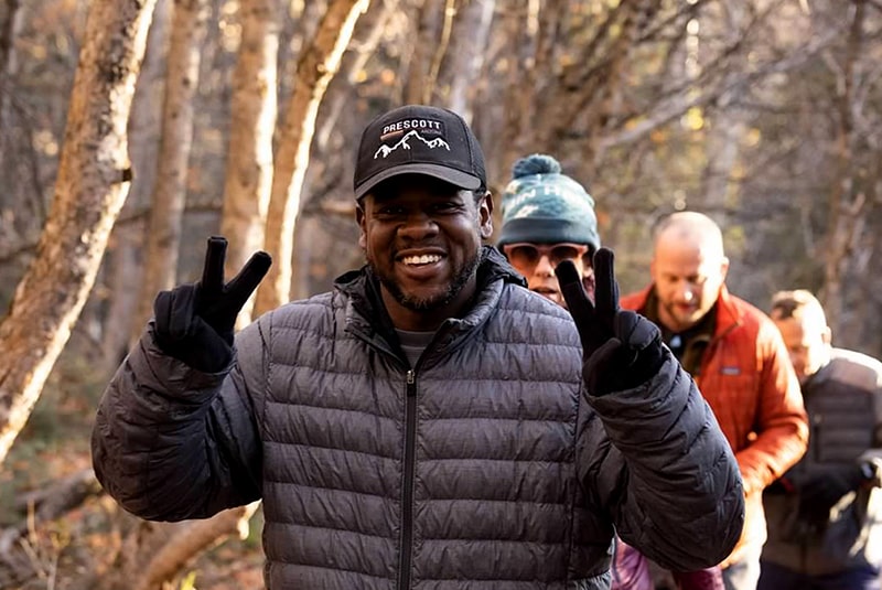 A male Coach on Stewart Falls hike signaling the peace sign with both hands, smiling.